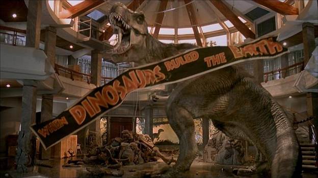 A production still of the T-Rex roaring in triumph as the “When Dinosaurs Ruled the Earth” banner falls from the ceiling to perfectly caption the moment