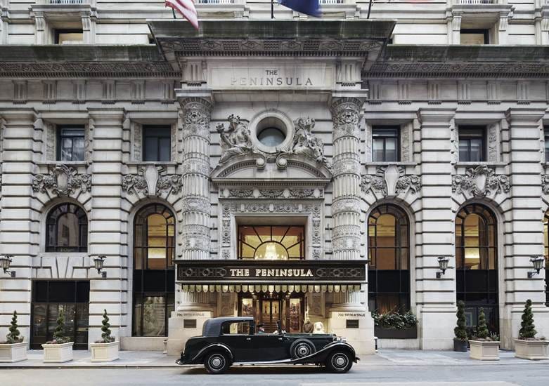 The entrance to the Peninsula Hotel. The facade of the building is ornate and is designed in a neoclassical style. The image is from: https://luxatic.com/new-yorks-appeal-is-complemented-by-the-peninsula-hotel/