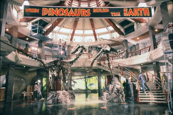 The same production still from Jurassic Park (1993) that appeared at the start of this post, showing the set for the interior of the visitors’ center. The interior is a rotunda featuring green marble floors; a curved, concrete staircase with red steel balusters; a mezzanine overlooking the first level; and concentric coffered windows decreasing in size as they approach the oculus.