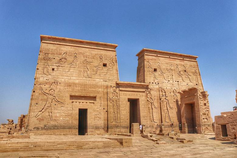 A photograph of the temple of Philae, showing a mastaba, or trapezoidal shape to the overall structure. The image is from: https://www.polyviajeros.com/templo-de-philae-guia-completa/#google_vignette
